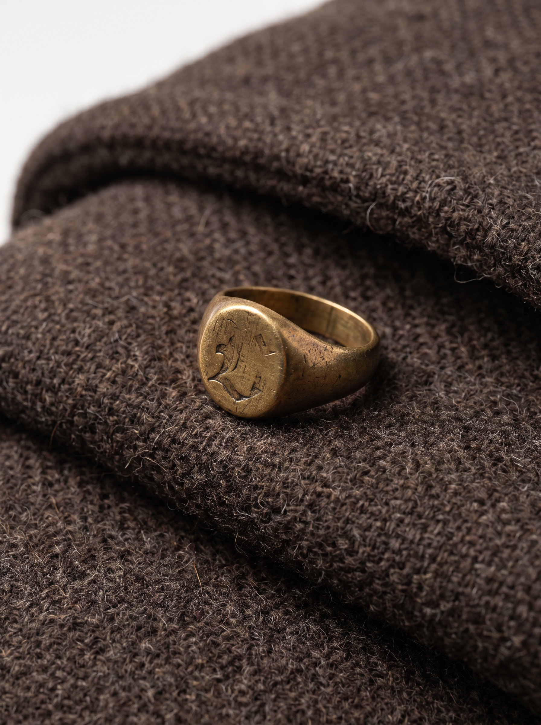 Macro detail shot of dark brown brushed wool coat fabric and antique brass signet ring.